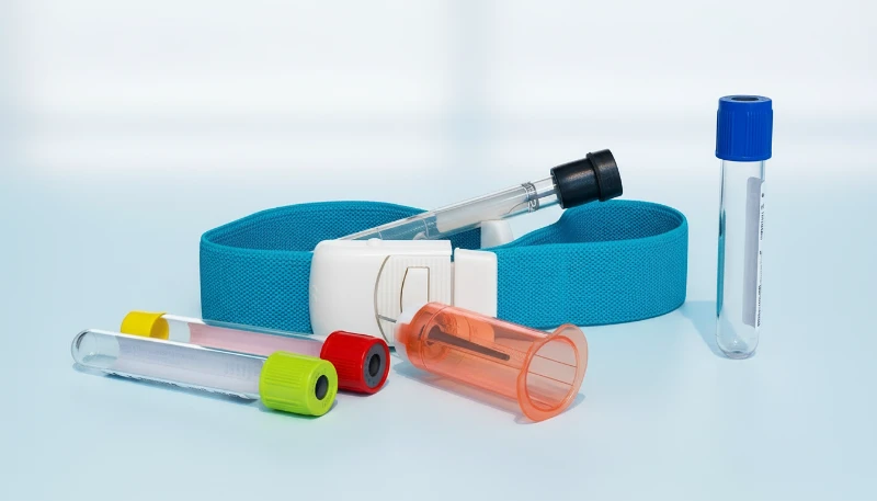 Medical tourniquet with multicolored vacutainer tubes on a light surface.
