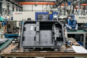 Large plastic component on table in injection molding factory with machinery and worker in background.