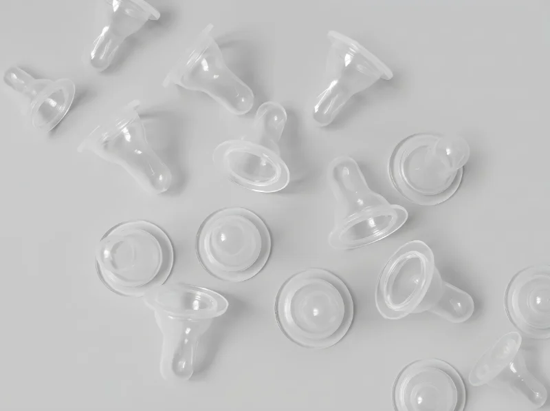 Clear plastic baby bottle nipples arranged on a plain surface, showcasing injection molded infant feeding components.